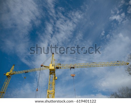 Building site with high-rise block under construction in an urban environment dominated by a large industrial crane silhouetted against a cloudy blue sky
