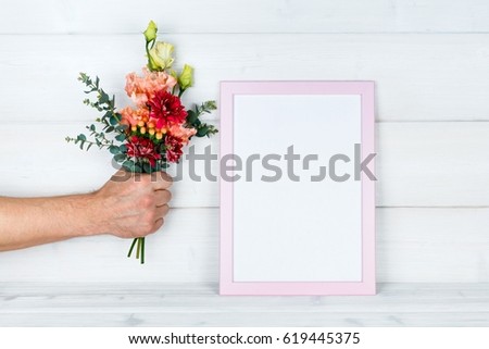Man's hand holding flowers and a photo frame on wooden background.Mockup with copyspace.
