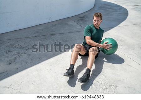 Medicine ball exercise russian twist man. Abs workout - fitness athlete working out doing exercises training oblique muscles on outdoor floor. Royalty-Free Stock Photo #619446833