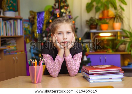 schoolgirl is sitting at table and thinks about the lessons