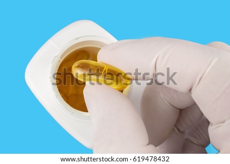 Hand in medical glove keeps yellow gel capsule of omega 3, fatty acid, fish oil, on blue background, white bottle, macro image