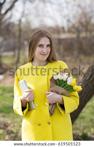 Cute cute girl with long hair in a yellow coat. Holds a tablet and a bouquet of flowers