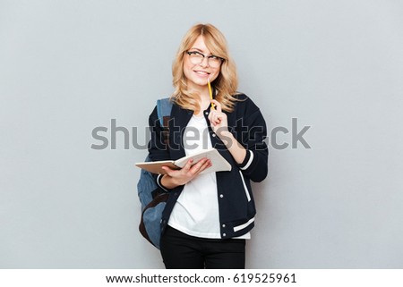 Smiling student in glasses holding notebook and pencil looking away