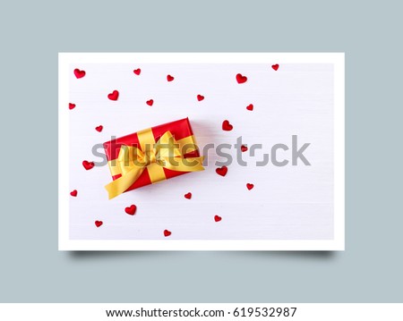 Gift box with red satin hearts. Present wrapped with yellow ribbon. Christmas or birthday package. On white wooden table. Photo frame design with shadow.