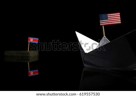 Origami boat with USA flag sailing towards North Korean flag isolated on black background