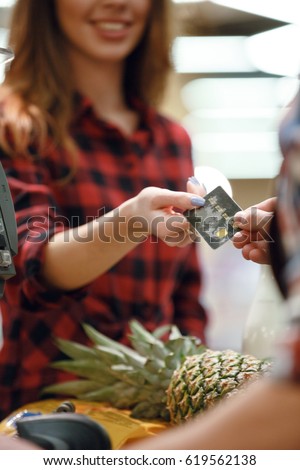 Cropped picture of young woman gives credit card to cashier man at workspace in supermarket.