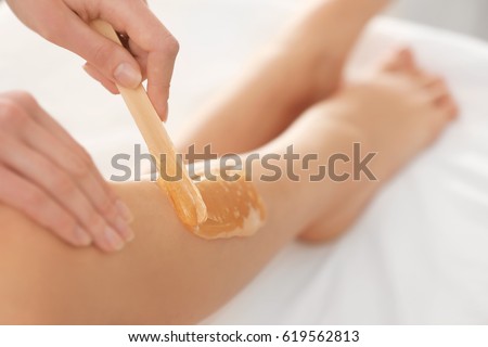 Beautician waxing female legs in spa center Royalty-Free Stock Photo #619562813