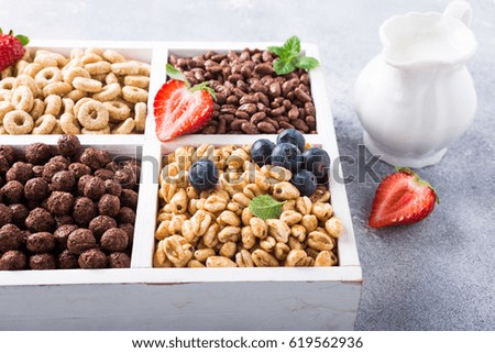 Milk jug and variety of cold quick breakfast cereals with berries in white wooden box, healthy eating concept, selective focus.