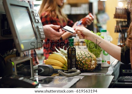Cropped picture of young man gives credit card to cashier lady at workspace in supermarket.