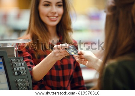 Picture of happy young lady standing in supermarket shop near cashier's desk holding credit card. Focus on card.