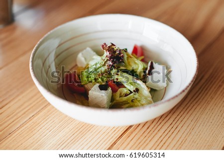 Pottery bowl with greek salad on wooden table