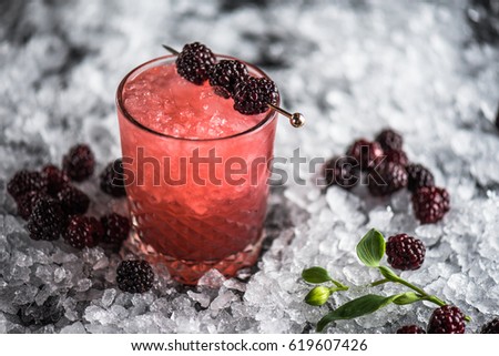 Cocktail in a glass, blackberry, blueberry and orchid flower on ice against a dark background. A close-up of a drink of fresh lemonade. Royalty-Free Stock Photo #619607426