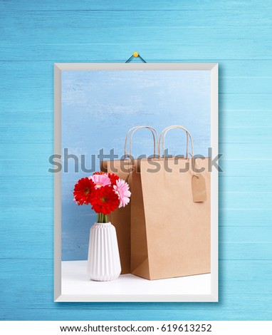 Mockup of blank shopping bags. Gerbera flowers in vase. Brown craft package. Concept for sales or discounts. Blue wooden rustic board. Photo frame on wooden rustic wall.