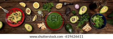 Delicious raw food with fresh slices of avocado, spinach soup, green salad, lemon and red wine on a long wooden table