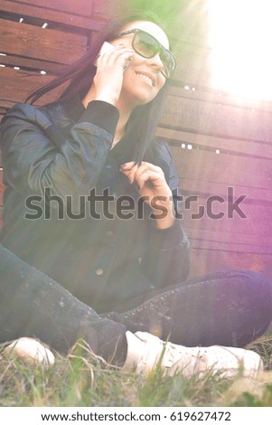 Teen girl sitting with mobile phone in hands on green lawn. Teenager. Hipster. Communication. On open air. Close-up.