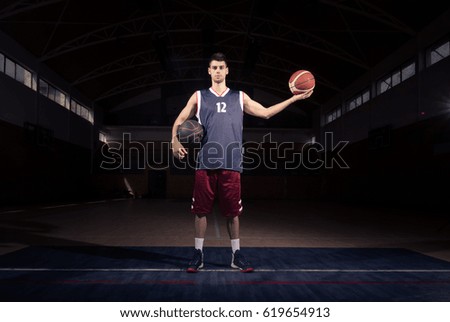 basketball player holding two balls, posing, dark basketball court indoors