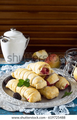 Homemade apple mini strudel with fresh apples, cherries, blackberries and sugar powder on a blue antique wooden background. Apple strudel in country style.