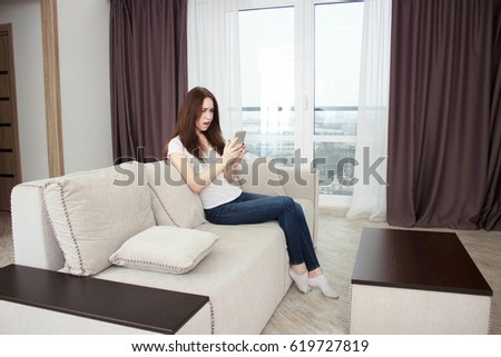 Happy girl reading a message in a smart phone sitting on a couch at home