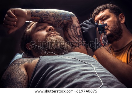 Professional tattooist making a tattoo in tatoo salon./Professional tattooist makes tattoo pictures in tattoo studio.