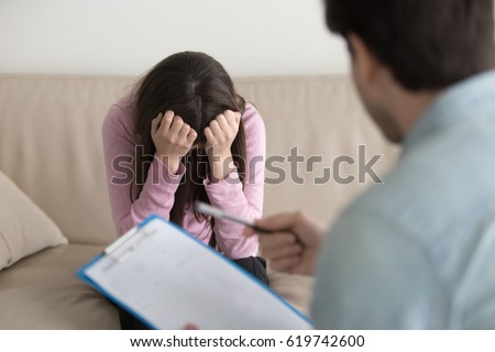 Young woman at the psychologist, feeling hopeless and depressed, crying holding her head in hands, upset teenage girl just found out about unwilling pregnancy or having disease Royalty-Free Stock Photo #619742600