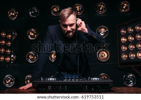 Young disk jockey with headphones and mixer checking equipment. Bearded professional DJ prepare to play famous music at nightclub dance party.