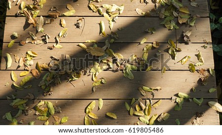 Low light picture of top view of brown wooden footpath or walk way in a mess of fallen dry leaves in the forest garden, the horizontal line of wood stripped and shadow of trees from sun light shading 