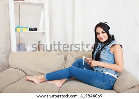 One relaxed girl resting and listening music with headphones sitting on a sofa in the living room at home with a warm light