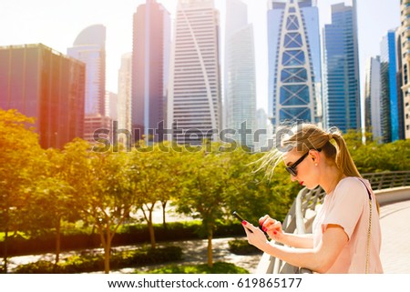 Blonde lady checks something in her iPhone standing on bridge before beautiful skyscrapers