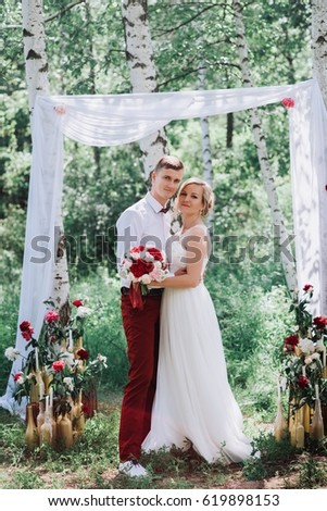 Young beautiful couple, bride and groom in the forest. Against the background of the wedding decor. This arch of fabrics and flowers.