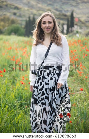 A young woman with a camera walking in the fields of poppies