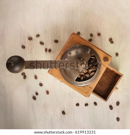 A square photo of a vintage coffee grinder, shot against the background of light wooden boards texture, with coffee grains and copy space, toned image