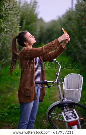 beautiful girl with a bicycle in an apple orchard,taking selfie with smart phone