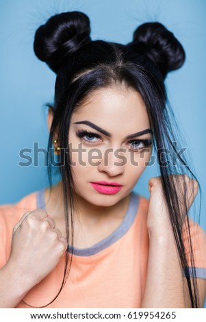 evil portrait of young brunette woman with fists on blue background