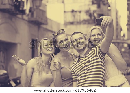 portrait of four young happy people taking self picture using mobile phone outdoors 
