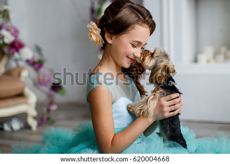 portrait of a beautiful young girl with blue eyes, with make up and hairstyle in a  lush turquoise dress with yorkshire terrier
