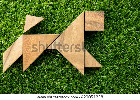 Wooden tangram puzzle in dog shape on artificial green grass background