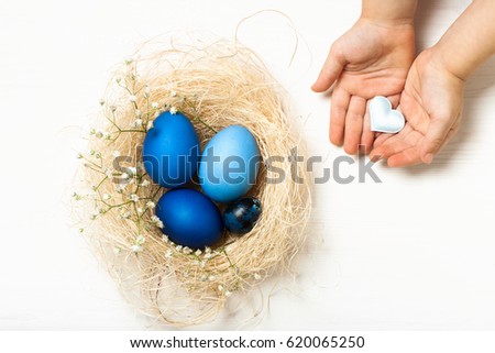 Easter eggs in blue colors in a nest and child's hands with hearts. The place for the text. The concept of stylish decoration for Easter, greeting cards, etc. Flat lay