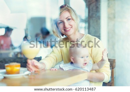 Smiling mother with baby girl looking through the window while having some drink in cafe