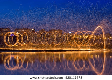 Hot Golden Sparks Flying from Man Spinning Burning Steel Wool near River with Water Reflection. Long Exposure Photography using Steel Wool Burning.