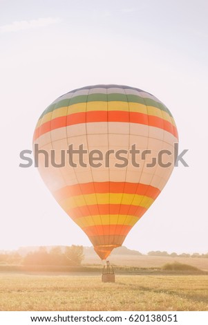The vertical photo of the huge orange and white air-balloon in the field during the sunset.