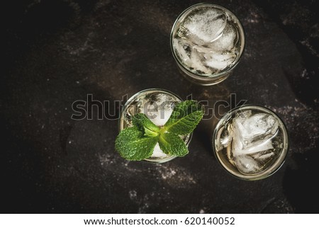 Alcohol cocktail made from golden tequila with ice cubes and mint. On a black concrete table. Copy space top view