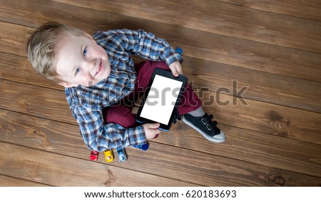 Boy using tablet and laptop while playing with toy cars on wooden floor at home. Tablet pc hero header image. Boy using ipad while lying on floor.