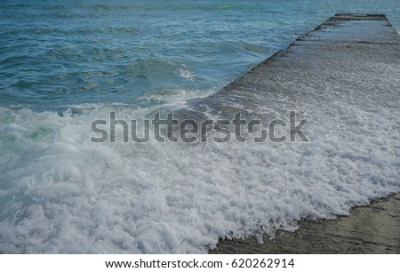 Ocean Wave Breaking on a Breakwall.  Turquoise blue ocean and a white wave breaking on a cement wall.