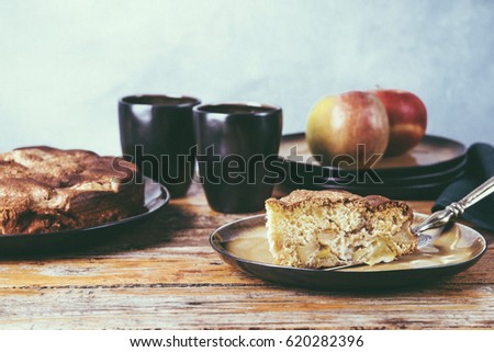 Piece of homemade apple pie, sponge cake "Charlotte" and ripe apples on the vintage wooden table. Selective focus. Retro toned image 