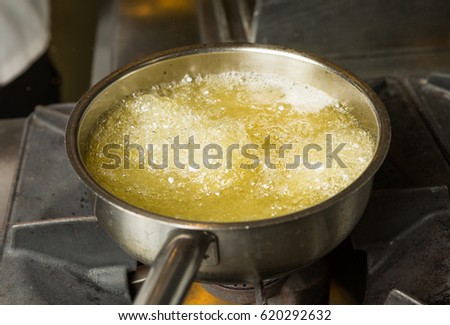 A pan of hot bubbling boiling oil in a silver pan on a hob. Royalty-Free Stock Photo #620292632