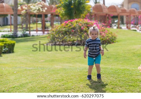 childhood and happiness, vacation. happy cute baby boy, small, little child with long blond hair in blue striped clothes playing on green grass in park on sunny summer outdoor on natural background