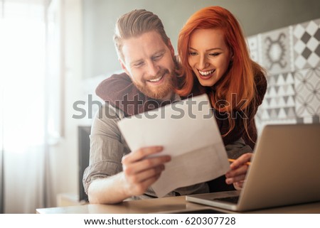 Photo of a positive young couple embracing and calculating the bills at home.