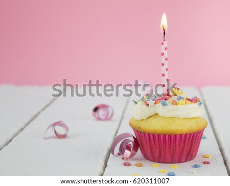 One cupcake with lit candle on white table against pink background - selective focus