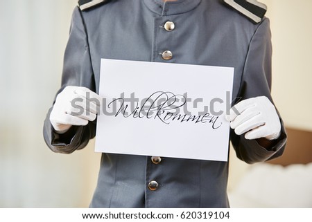 Hotel clerk holding German sign saying "Willkommen" (welcome)