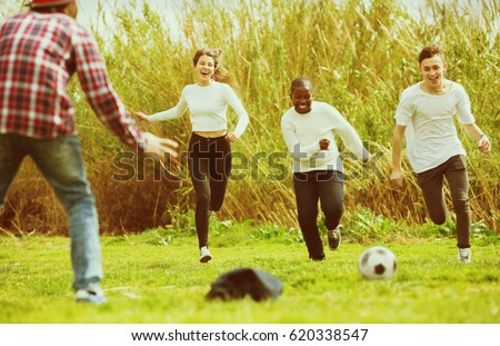 Portrait of happy laughing four friends posing on countryside field with ball in sunny day